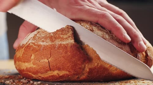 Person Cutting Loaf of Fresh Bread With Knife