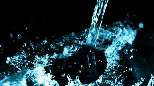 A stream of water falls and creates a splash on a black background. Slow motion.