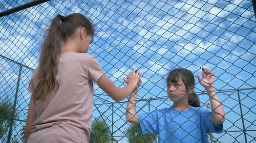Girls Hold Hands Through Chain Link Fence