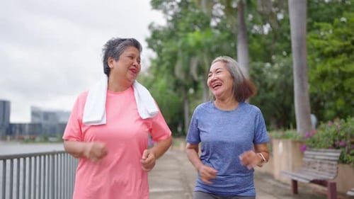 Two happy Asian senior women jogging exercise outdoors in modern city.