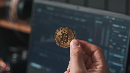 Hand Holding Bitcoin in front of Stock Charts