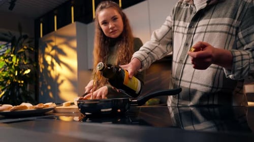 Primer plano de una joven pareja enamorada en una hermosa cocina preparando la cena juntos, el chico vierte aceite