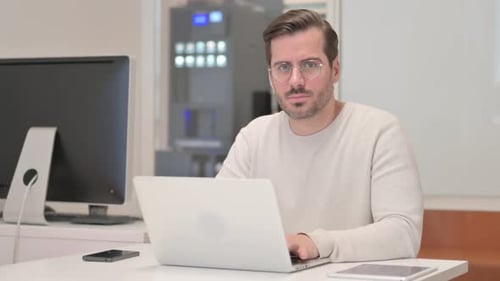 Schockierter junger Mann blickt bei der Arbeit in die Kamera