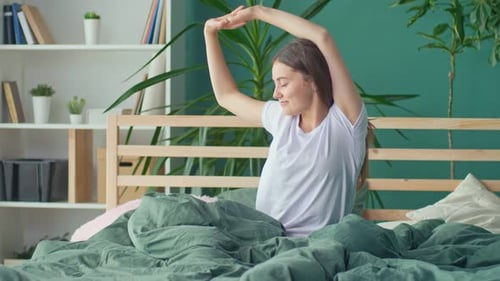 A Happy Young Woman Wakes Up in a Happy Mood Stretching Cheerfully in Bed