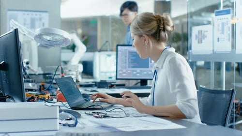 Female Computer Scientists Connects Circuit Board to Her Laptop with Mock-up Green Screen. She Work