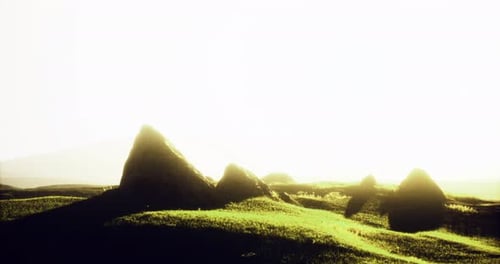 Sunlight Brightens Grassy Hills and Distant Rock Formations