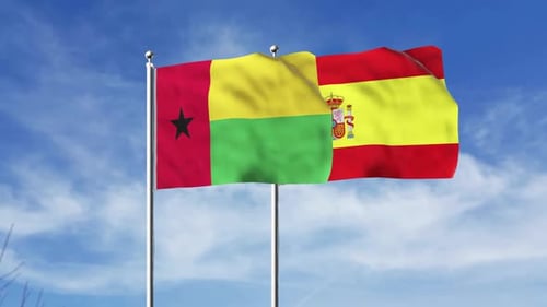 Guinea-Bissau and Spain Flags Waving in Blue Sky