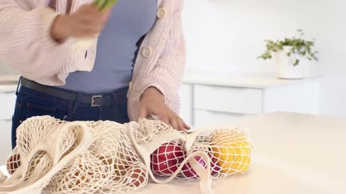 Mujer en la cocina sosteniendo brócoli, desempacando la comida de una bolsa reutilizable