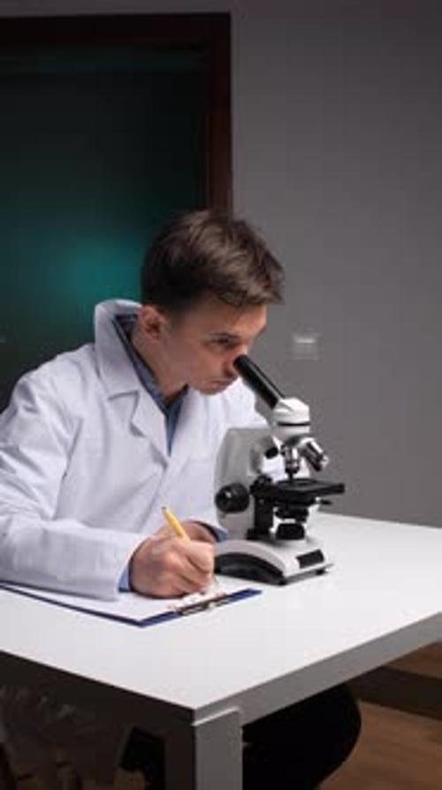 Young Man Using Microscope and Taking Notes
