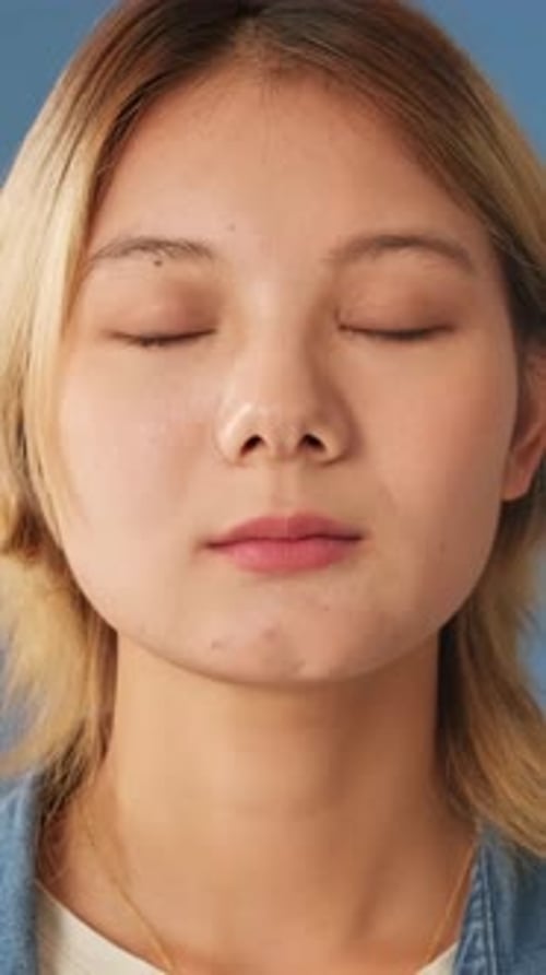 Close-up, smiling woman opens eyes and looks at camera isolated on blue backgroundin studio