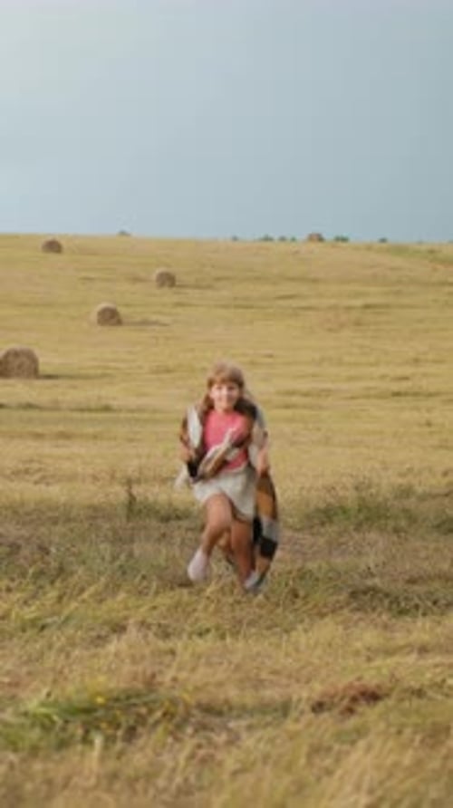 Little Girl Running With Blanket in Open Field Under Cloudy Sky