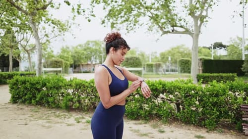 Woman Running and Checking Smartwatch in Urban Park
