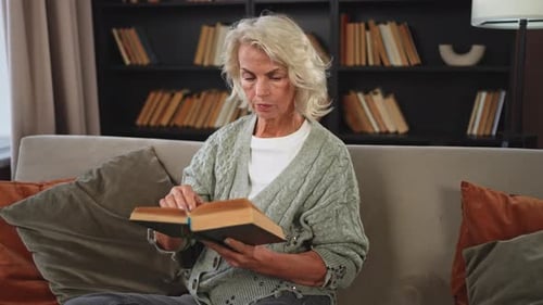 Senior Woman Reads Book on Couch at Home