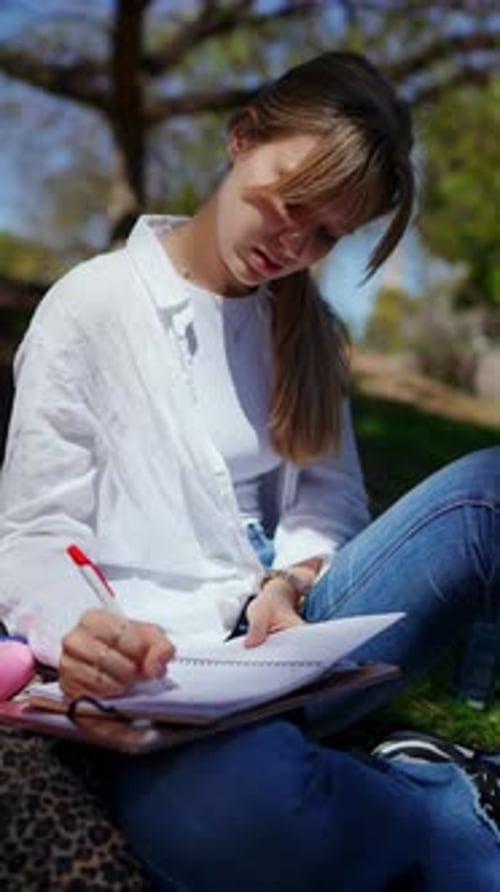 Woman Writing in Notebook Outdoors on Sunny Day