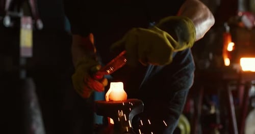 Professional blacksmith forging red hot metal on anvil in dark workshop
