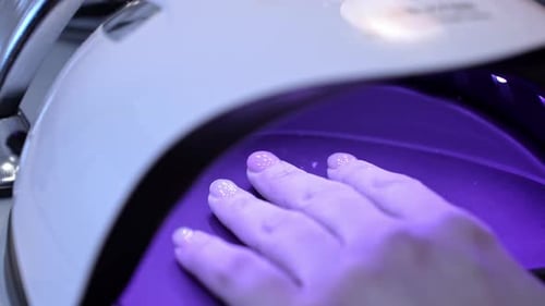 Close-up of a hand curing glossy gel polish under a UV nail lamp, highlighting professional