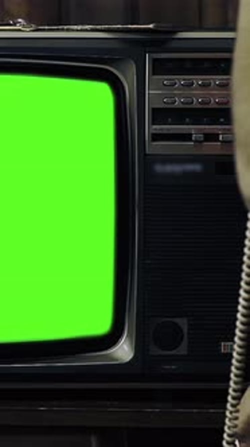 Man Holding 80s Phone While Turning On Old TV with Green Screen in a Dimly Lit Room - 4K Vertical