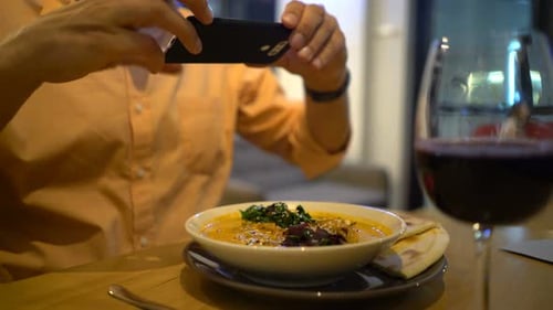 Young Man Taking Photo of Food with Cellphone Sitting at Restaurant 30s