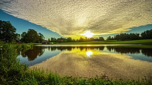 Golden Sunlight And Cloudscape Reflected Over Still Water Surface Of A Lake During Sunrise. Timelaps