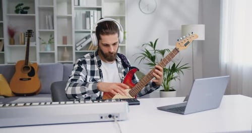 Músico caucásico, hombre con auriculares, crea música electrónica en sintetizador, piano y guitarra electrónica.