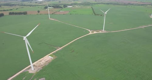 Wind turbines in green fields on overcast day, hinting at renewable energy sources, aerial view
