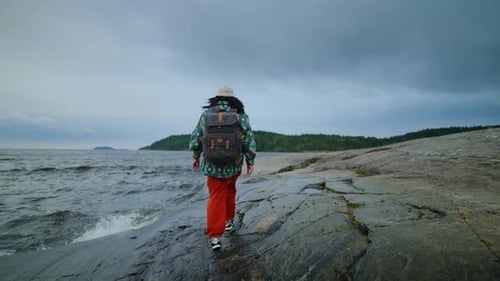 Woman Tourist With Backpack Walking On Stone Shore Of Sea Or Lake In Cloudy Weather SlowMotion