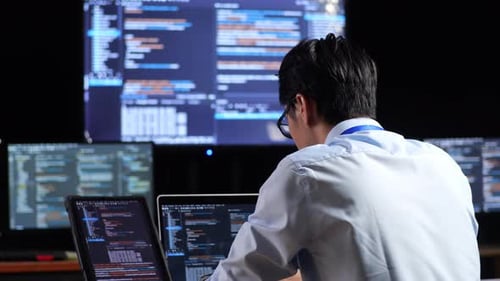 Programador examinando o banco de dados no tablet e escrevendo código em um laptop usando vários monitores