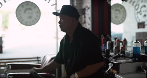 Professional Asian Male Barber Shaking and Folding Black Protective Cape in Interior