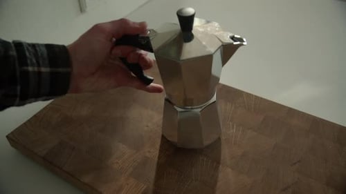 Joven hipster colocando el café Bialetti Moka Express en una tabla de cortar de madera por la mañana en el Reino Unido