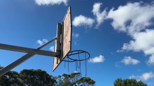 Ein Basketball-Backboard und ein Korb, von unten betrachtet, mit dem Himmel und einigen Wolken im Hintergrund.