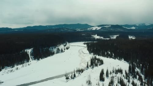 Mountain covered with snow, forest and meandering stream. Aerial panoramic