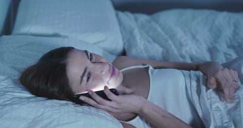 Woman Laughing on Mobile Phone in Bed at Night