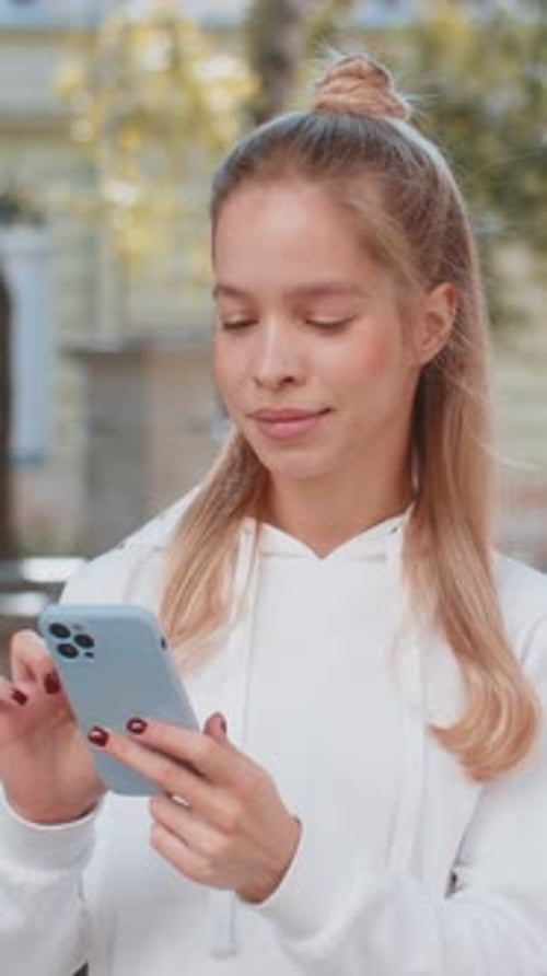 Happy Caucasian Woman Using Smartphone Typing Text Messages Browsing Internet on City Town Street