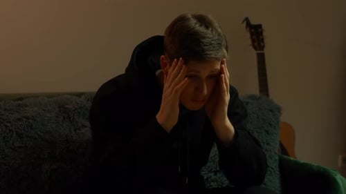 Jeune homme caucasien souffrant d'un stress sévère, avec une guitare debout en arrière-plan