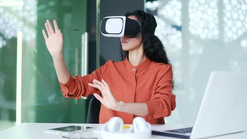 Young female employee works using VR glasses in virtual reality simulator while sitting at workplace