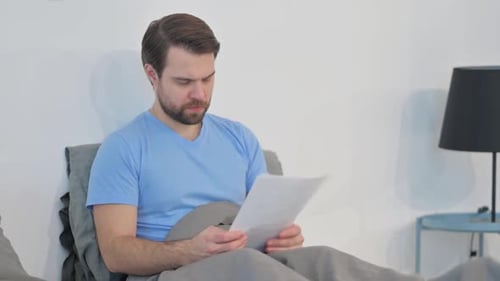 Man Reviews Documents in Bed in a Bedroom