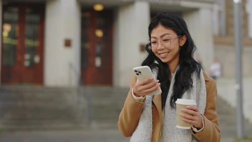 Smiling Woman Checks Phone Holding Coffee Outside