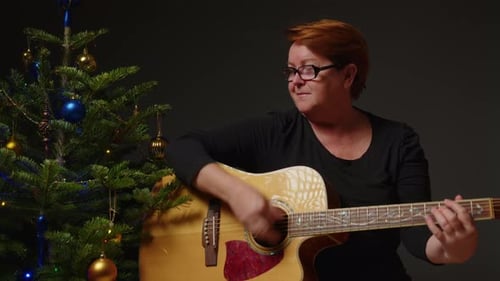 Woman Plays Guitar Next to Christmas Tree