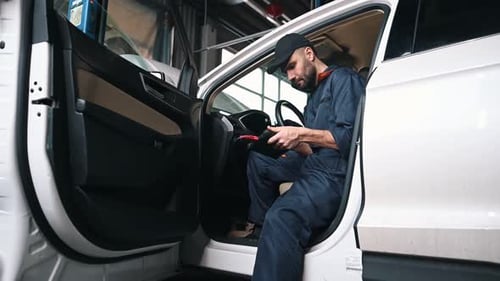 On the seat, with digital tablet. Mechanic working in a car service station.