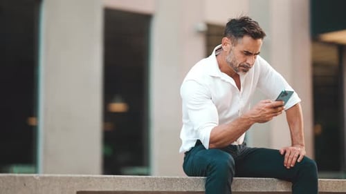 Man Using Smartphone Sitting in an Urban Setting