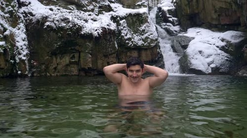 Man Swims in Cold Water by Waterfall