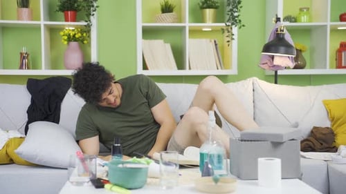 Young Adult Stretching on Sofa in Messy Interior