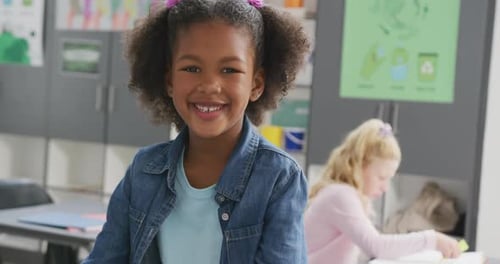 Video portrait of happy biracial schoolgirl smiling in school classroom