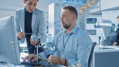 Wirtschaftsingenieurin spricht mit Elektronikspezialistin, sie hält einen Prototyp einer Metallkomponente in der Hand