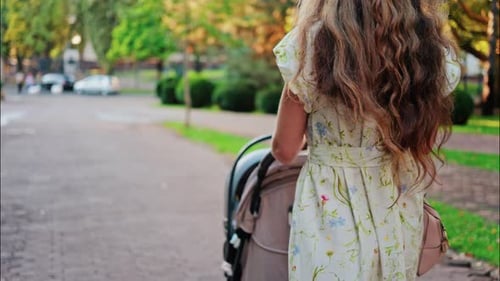 A woman in a floral dress pushing a baby stroller along a park path