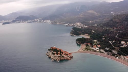 AERIAL - Sveti Stefan island, tombolo, and Villa Milocer in Montenegro, reverse