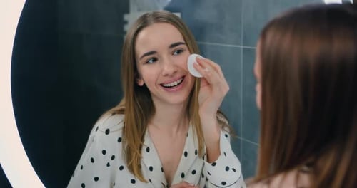 Young Woman Cleans Face in Bathroom Mirror