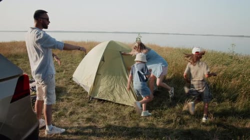 Family Setting Up Tent Near Tranquil Lake