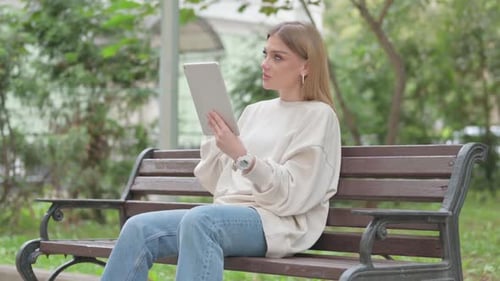 Casual Young Woman Doing Video Chat on Tablet while Sitting Outdoor on a Bench