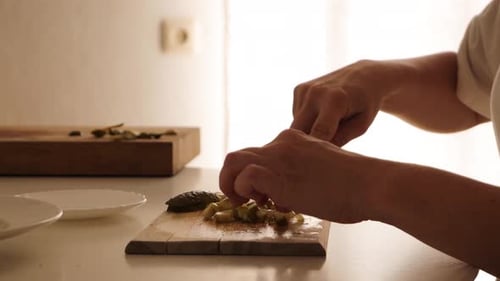 Close-up of a woman skillfully slicing pickled cucumber on a wooden cutting board.